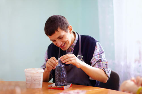 young adult man with disability engaged in craftsmanship on practical lesson, in rehabilitation center